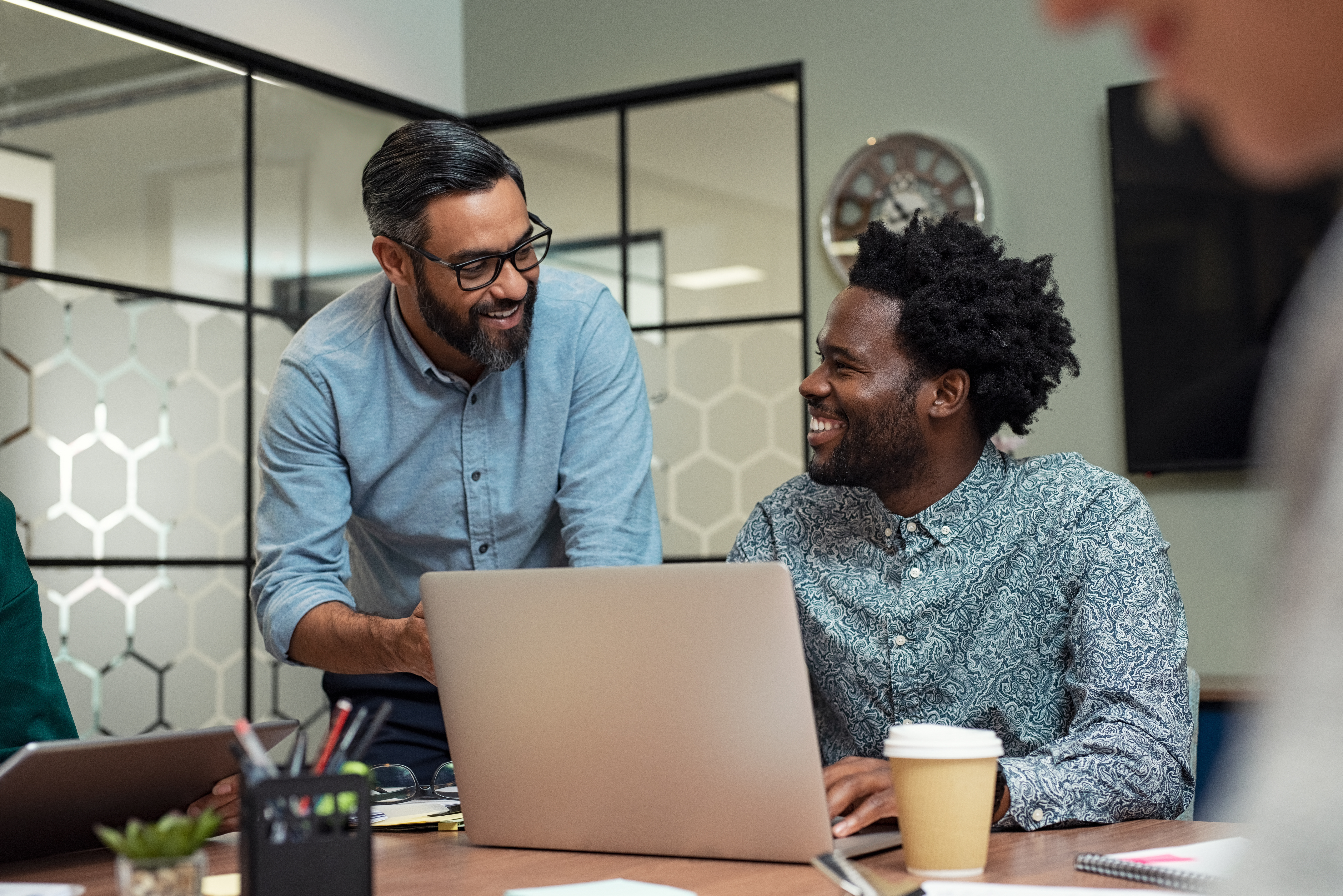two guys, one standing one seated, discussing over a laptop