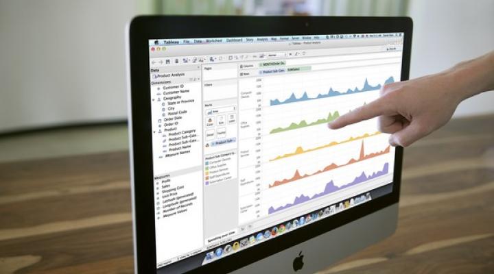 Tableau software running on an Apple monitor with a hand pointing to the screen.